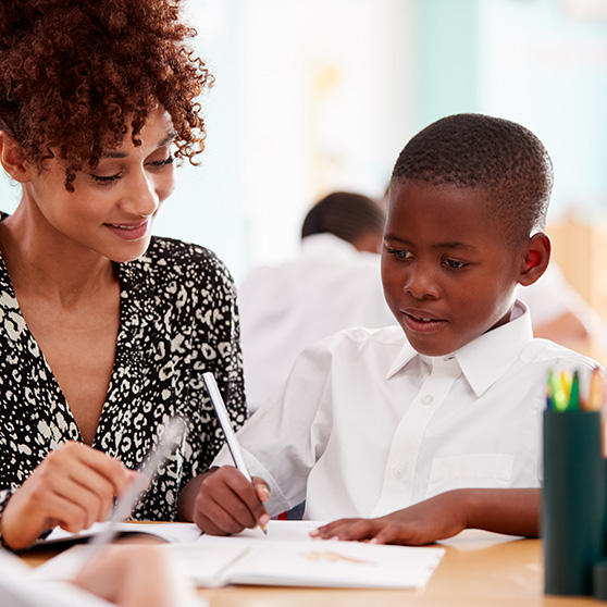 Woman Elementary School Teacher Giving Male Pupil a support to easily learn