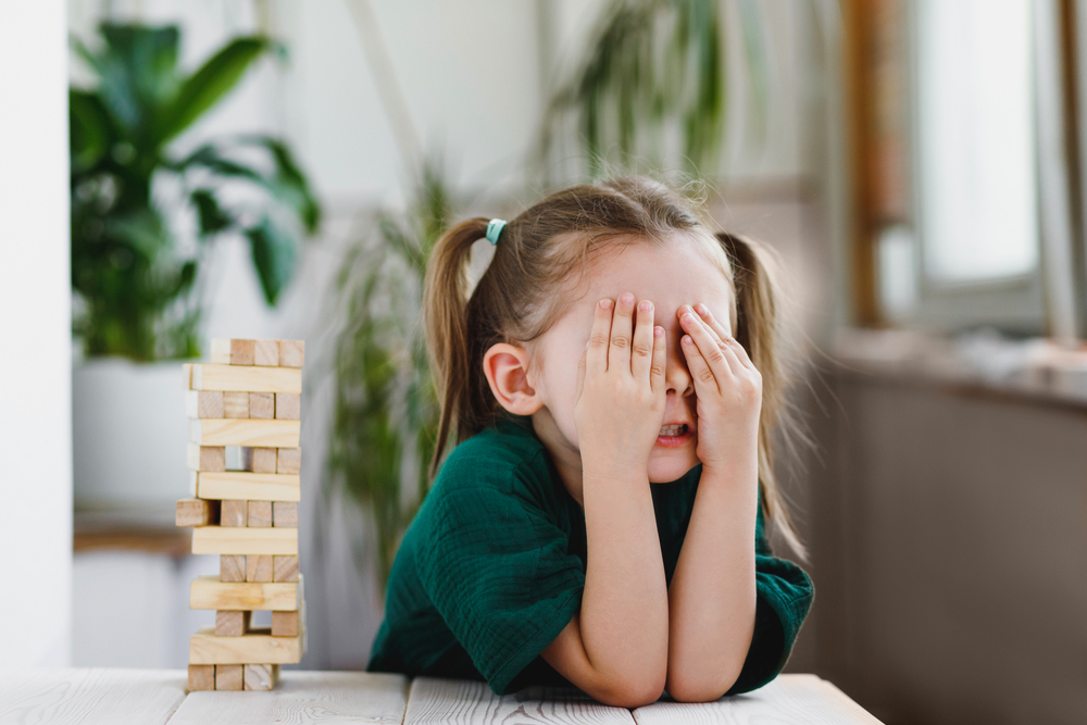 Young girl covering her face while playing with wooden blocks.