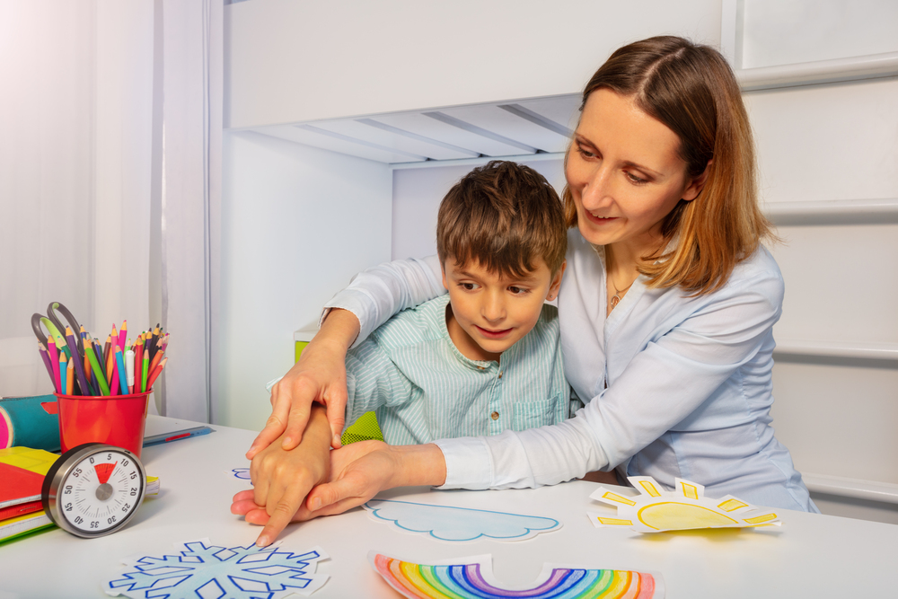 Therapist guiding young child with art activities at a table.