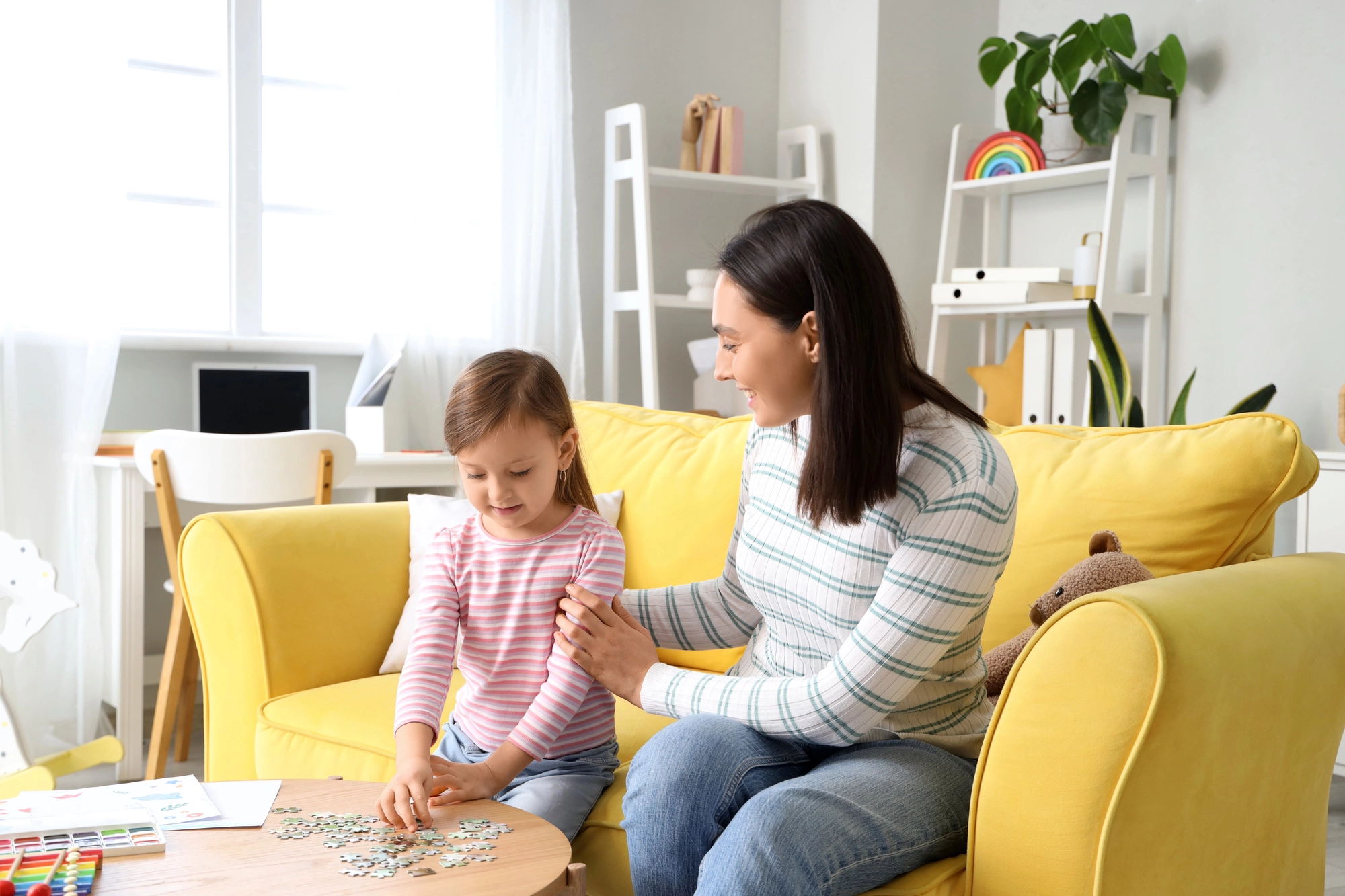 Woman helping a young girl with a puzzle on a table.